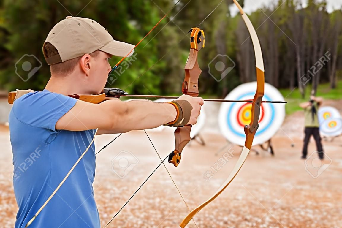 young man doing archery, aiming at the target, fun outdoor activity concept