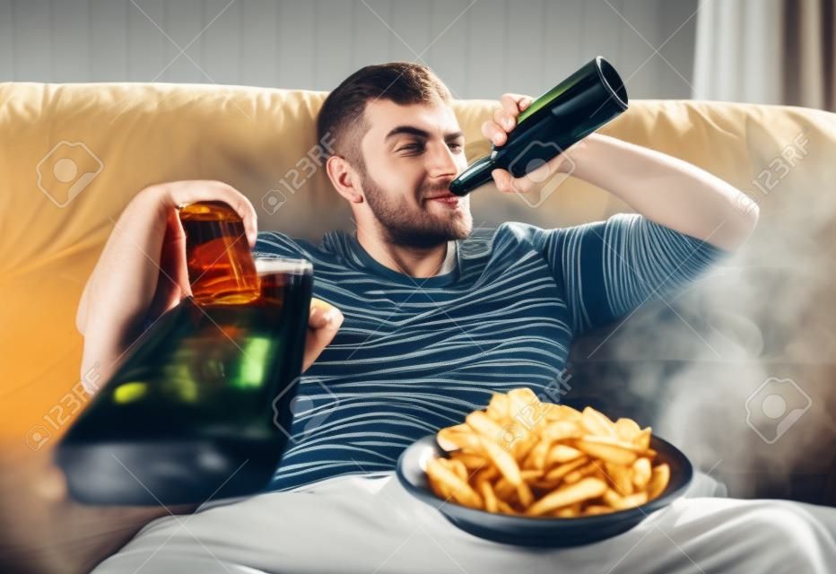 Homme avec de la bière et des chips en regardant la télévision à la maison