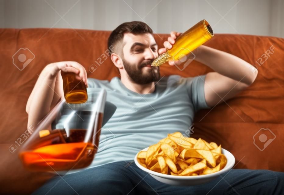 Homem com cerveja e batatas fritas assistindo TV em casa