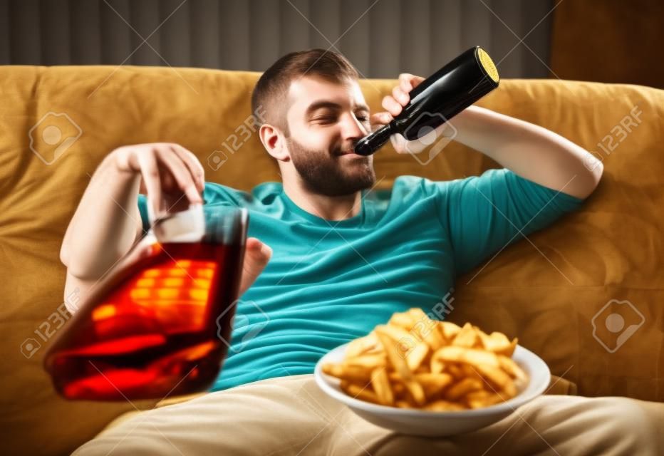 Homem com cerveja e batatas fritas assistindo TV em casa