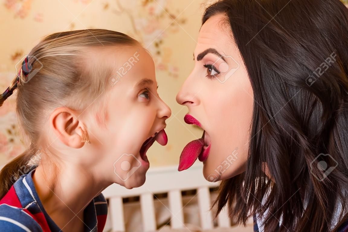 Young mother and the little girl show each other tongues. Family fool around concept.