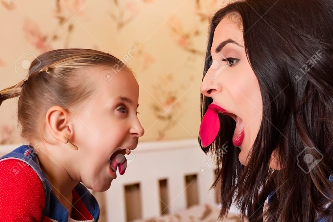 Young mother and the little girl show each other tongues. Family fool around concept.