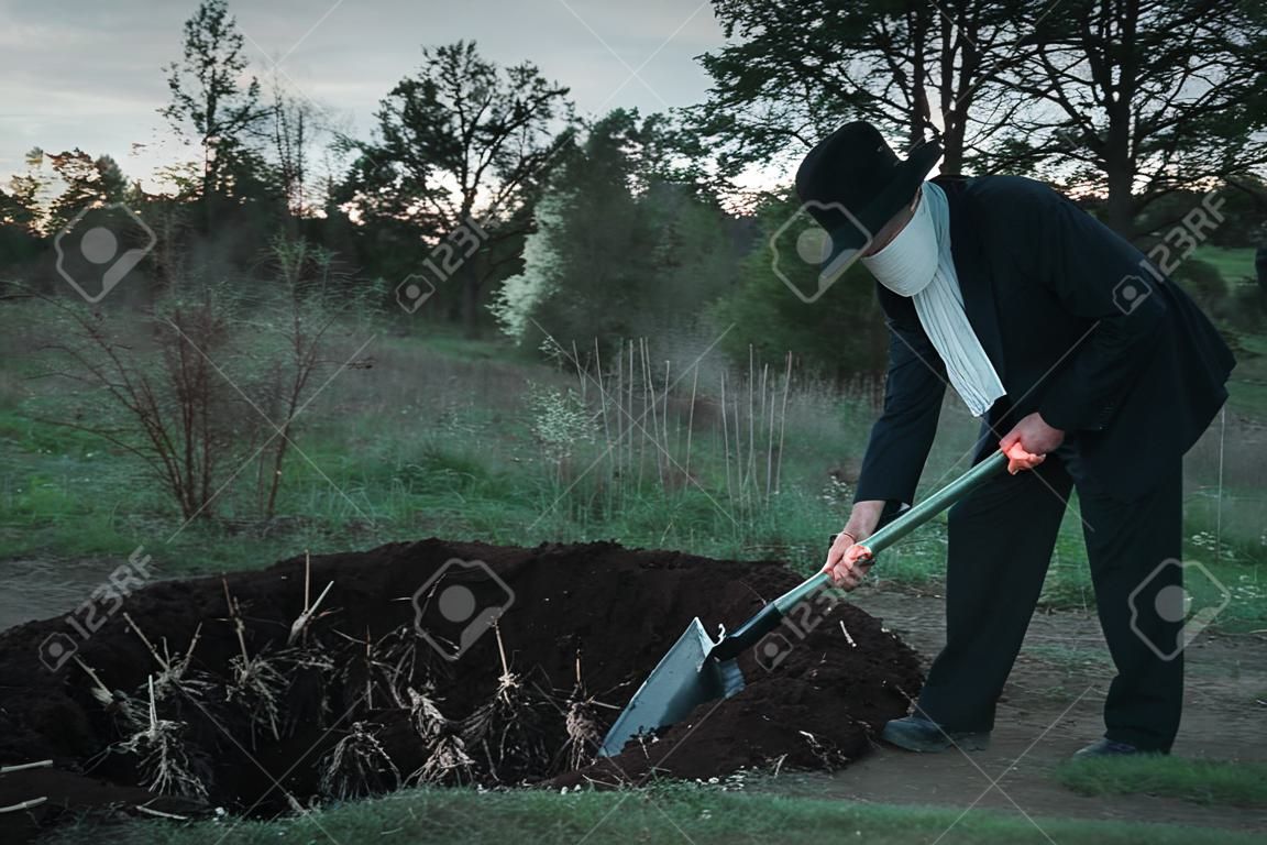 Bloody murderer is digging a grave for the victim