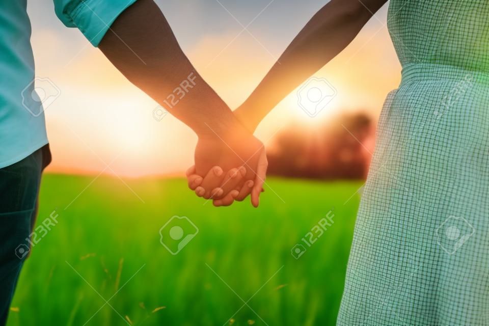 Couple hold hands in green field on sunset