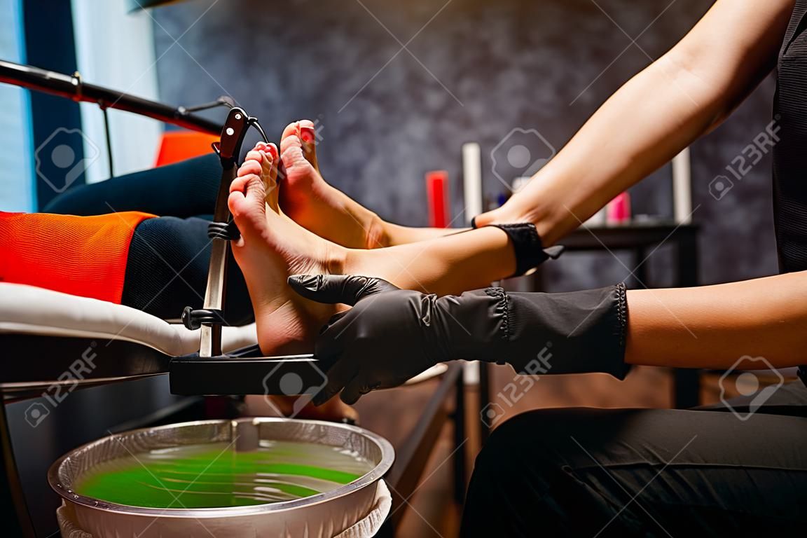 Fußpfleger in schwarzen Handschuhen reibt die Creme