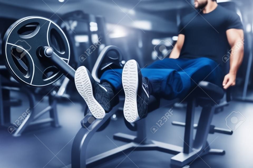 Male person trains legs on exercise machine in gym