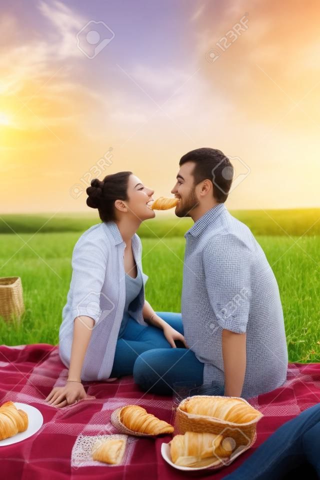Couple eating croissants on picnic in summer field