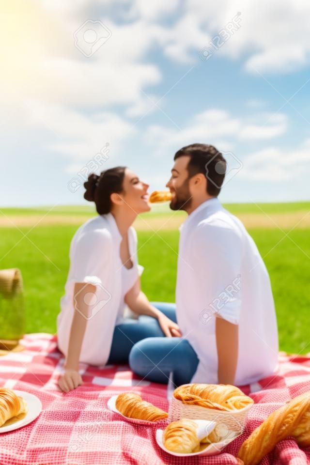 Couple eating croissants on picnic in summer field