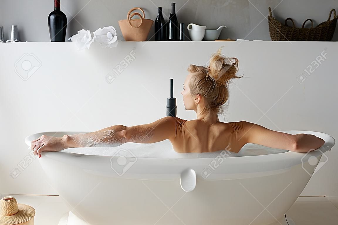 Rear view on woman drinking wine in bath