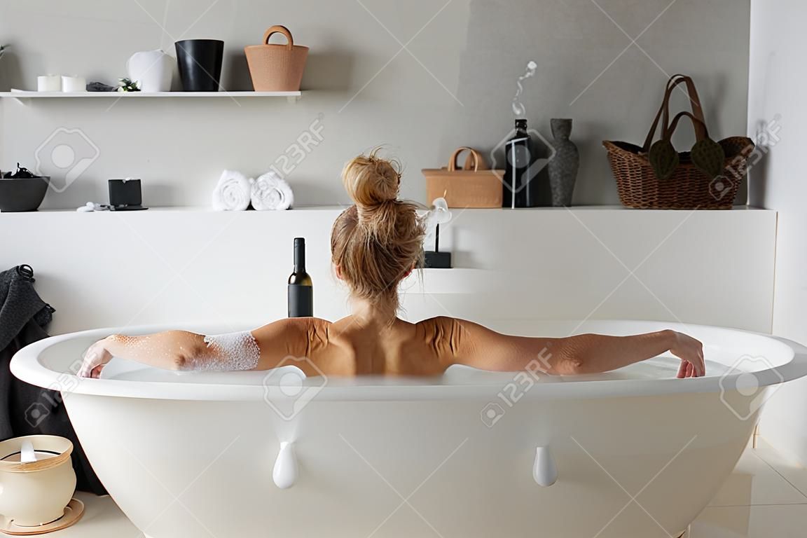 Rear view on woman drinking wine in bath