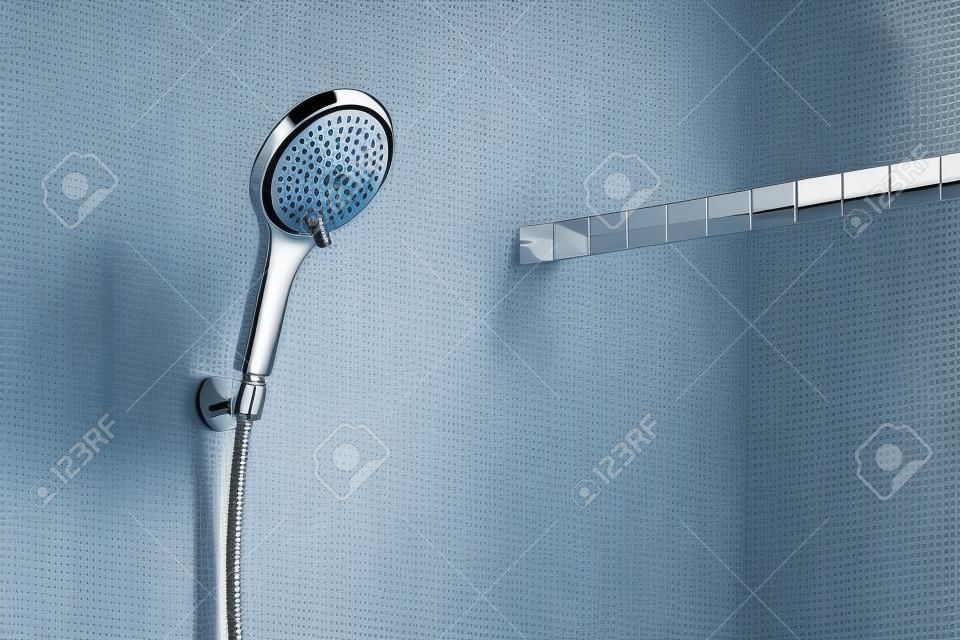 Modern shower head is hanging against the bathroom wall close up.