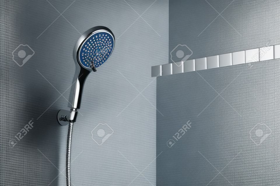 Modern shower head is hanging against the bathroom wall close up.