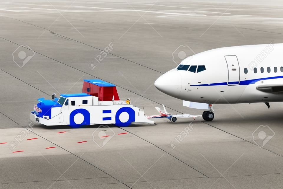 samolot na pasie startowym lotniska z ciągnikiem pushback podłączonym do holowania podwozia samolotu przez pojazd naziemny do bramy terminalu.