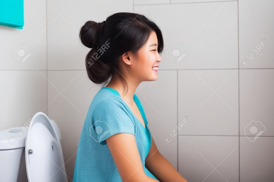 Молодая азиатская женщина, сидящая на унитазе дома с счастьем