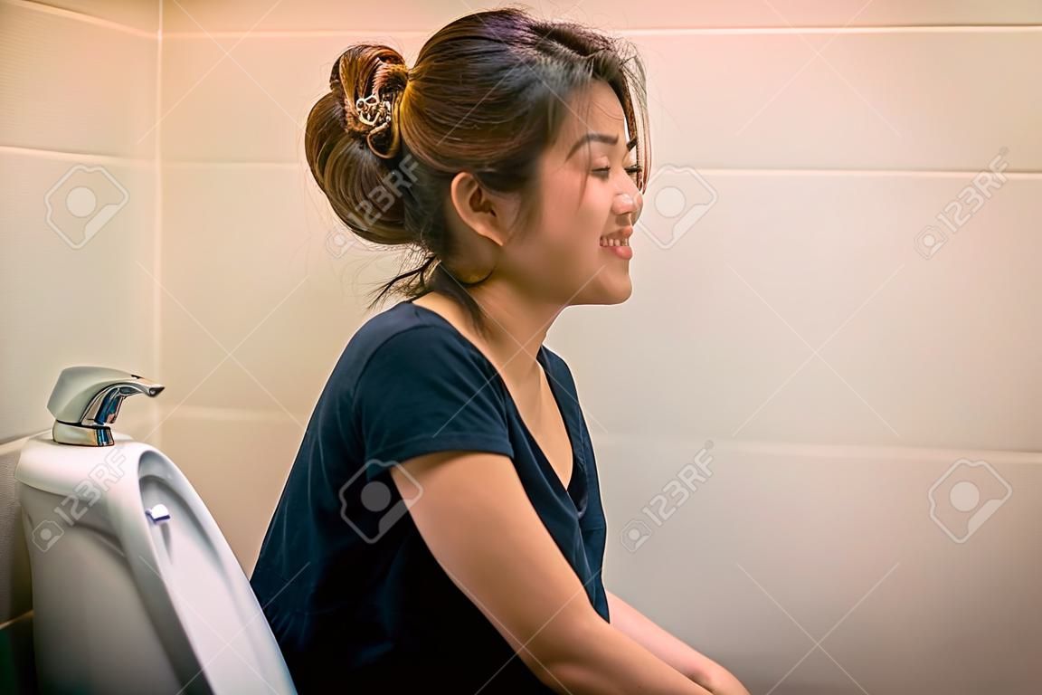Молодая азиатская женщина, сидящая на унитазе дома с счастьем