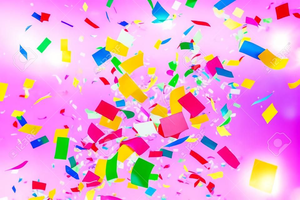 Colorful confetti and ribbons flying in the air on a pink background