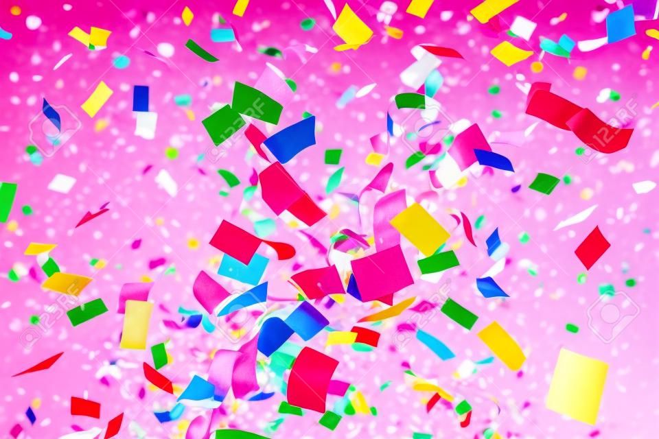 Colorful confetti and ribbons flying in the air on a pink background