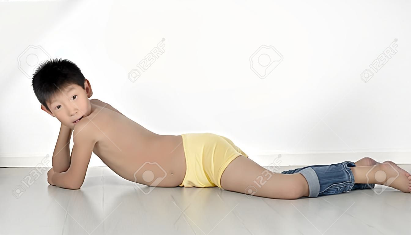 Asian shy boy with underwear and jeans laying on gray floor.