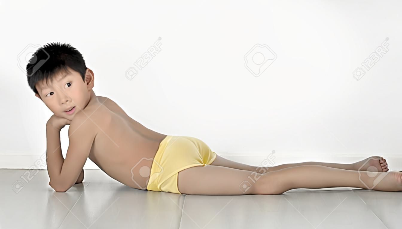 Asian shy boy with underwear and jeans laying on gray floor.