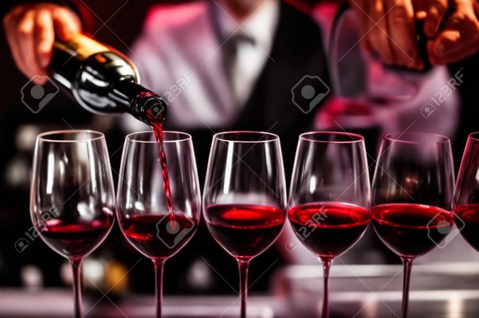 Barman nalewa czerwone wino do kieliszków przy barze męski sommelier nalewa czerwone wino do kieliszków na długich nóżkach