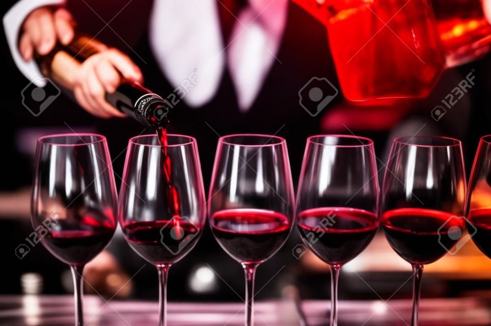 Barkeeper gießt Rotwein in Gläser an der Bar. Männlicher Sommelier gießt Rotwein in langstielige Weingläser.