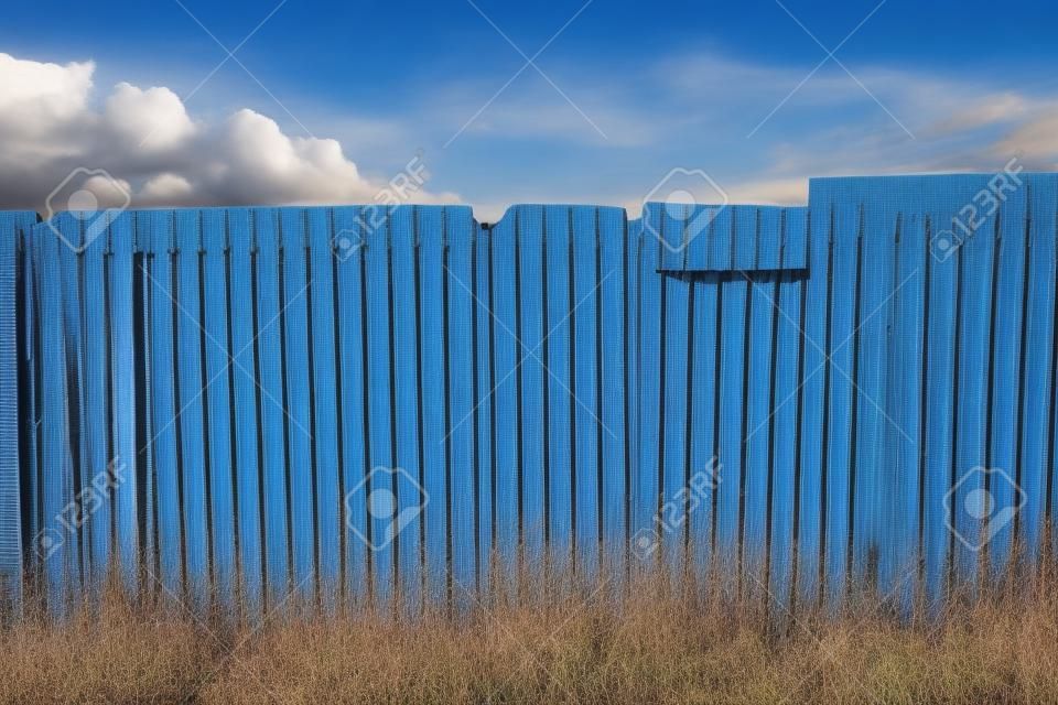 Rusty galvanized corrugated fence with the blue sky and cloudy