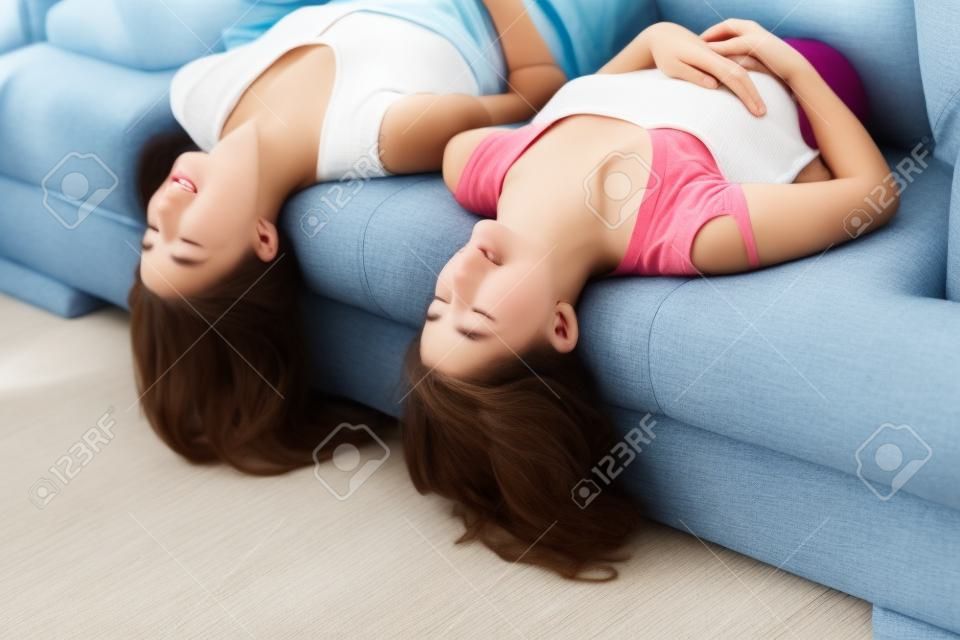 Happy teen girls lying on couch upside down, listening to music, eyes closed.�