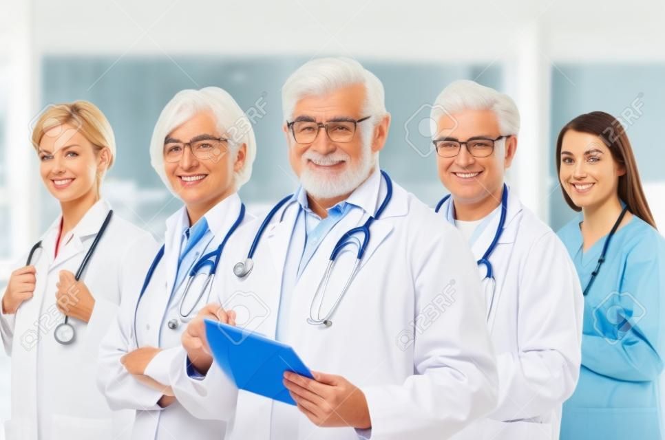 Team of medical professionals lead by senior white haired doctor looking at camera, smiling.