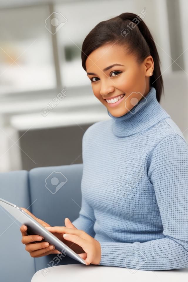 Smiling young woman using tablet pc, looking at camera.�