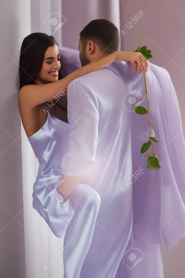 Romantic couple embracing at home, woman in silk nighty holding rose.�