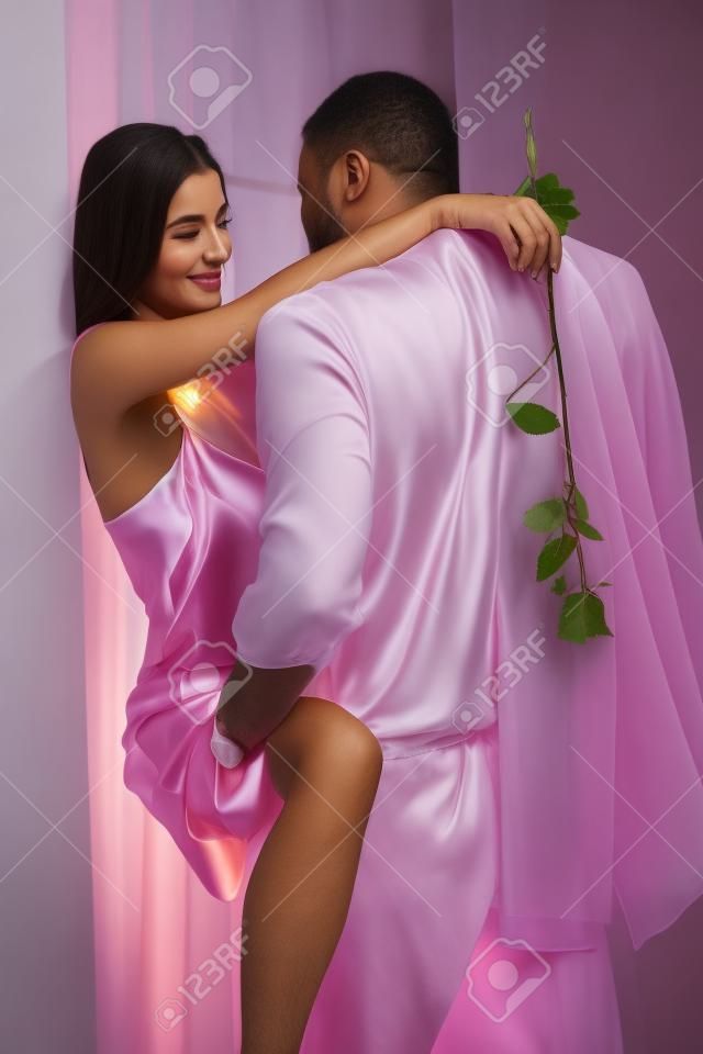 Pareja romántica abrazando a su casa, la mujer en camisón de seda rosa celebración.