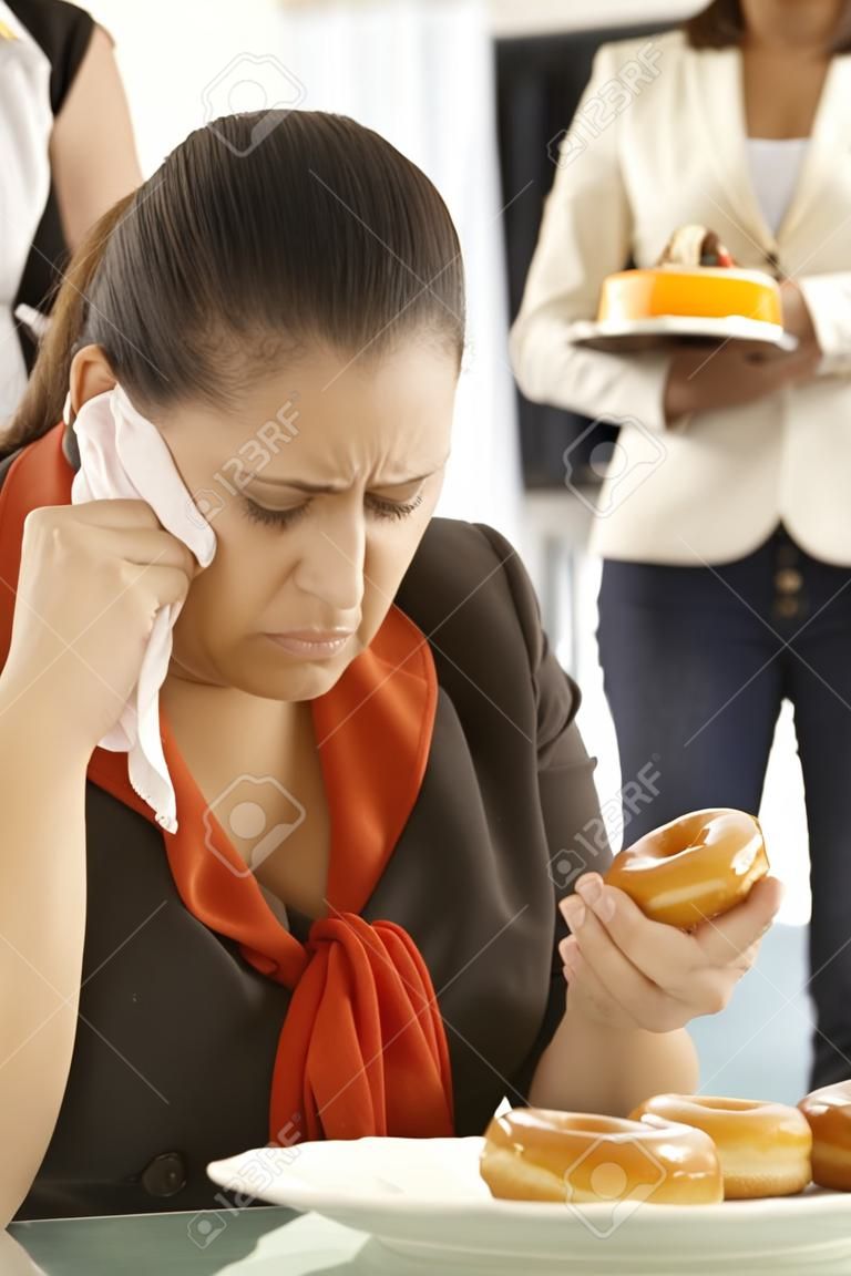 Employé de bureau malheureux assis à son bureau, pleurer, manger beignet.