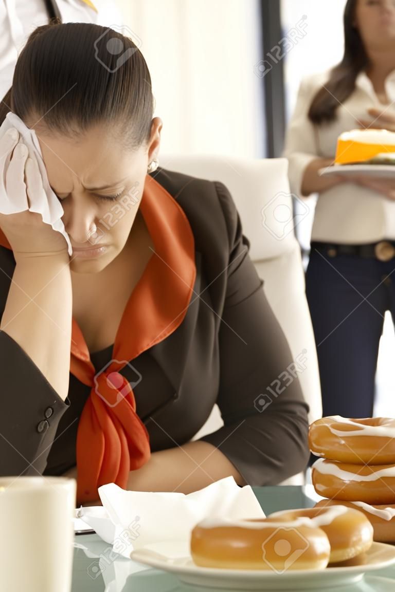 Employé de bureau malheureux assis à son bureau, pleurer, manger beignet.