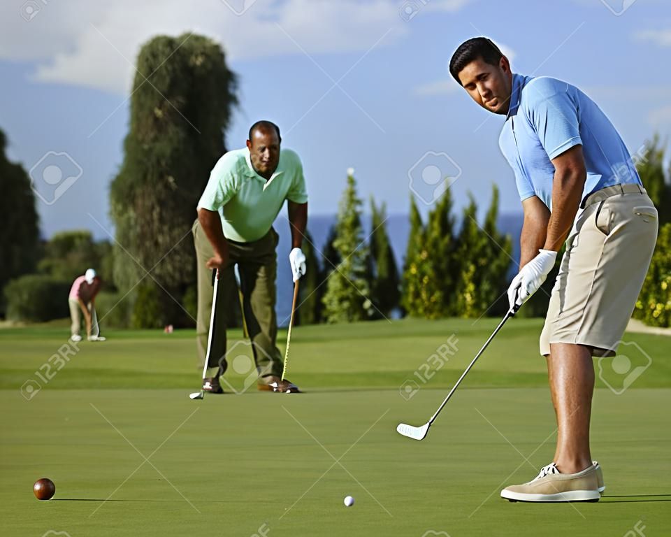 Giovane maschio golfista messa palla sul green della buca.