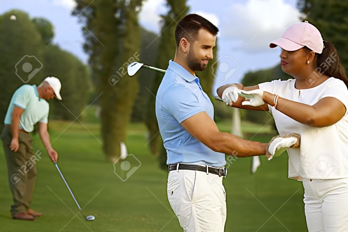 Женский гольфист обучения игры в гольф, мужской инструктор помогает.