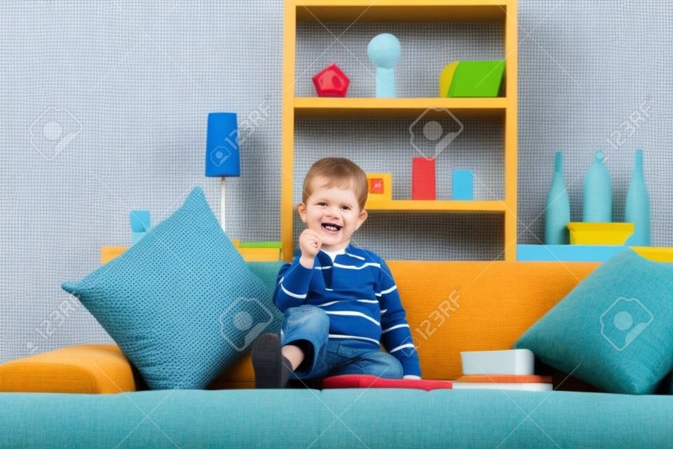 Bambino felice caucasica con i giocattoli, seduta sul divano, guardando alla fotocamera, sorridente. Chiuso Home.