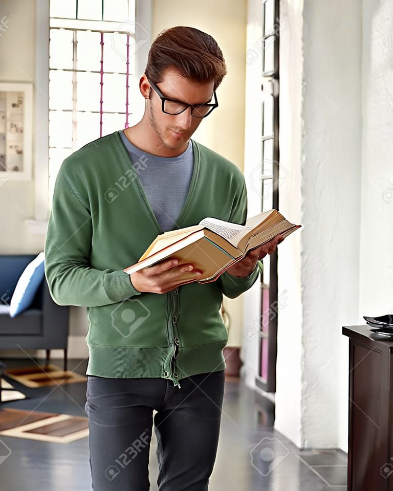 Stylish young man standing at home, reading book.