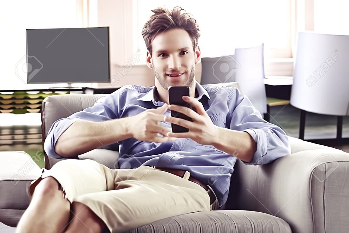 Happy man sitting in armchair at modern loft home using mobile phone.