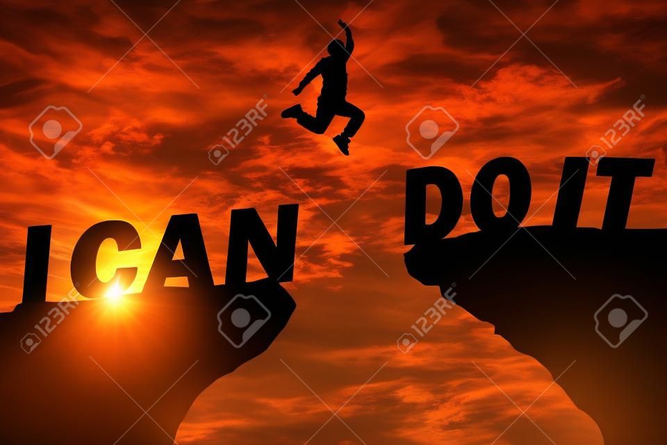 Fundo do pôr-do-sol da silhueta. Um homem está pulando sobre a falésia e saltar entre"eu posso fazê-lo "palavra. Esta foto mostra sobre a liberdade, ativo e bem sucedido, foto silhueta e ideia de conceito ativo.