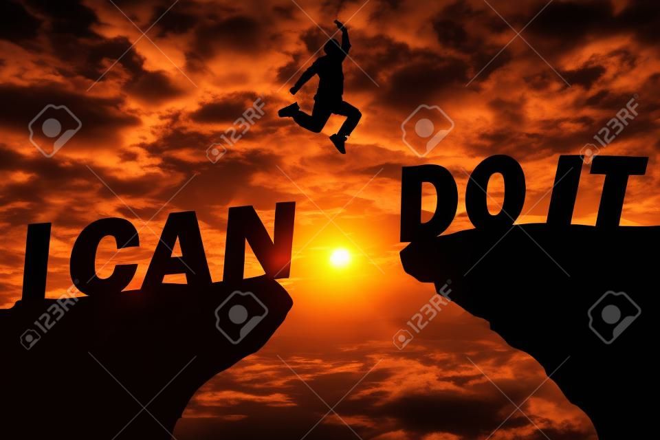 Fundo do pôr-do-sol da silhueta. Um homem está pulando sobre a falésia e saltar entre"eu posso fazê-lo "palavra. Esta foto mostra sobre a liberdade, ativo e bem sucedido, foto silhueta e ideia de conceito ativo.