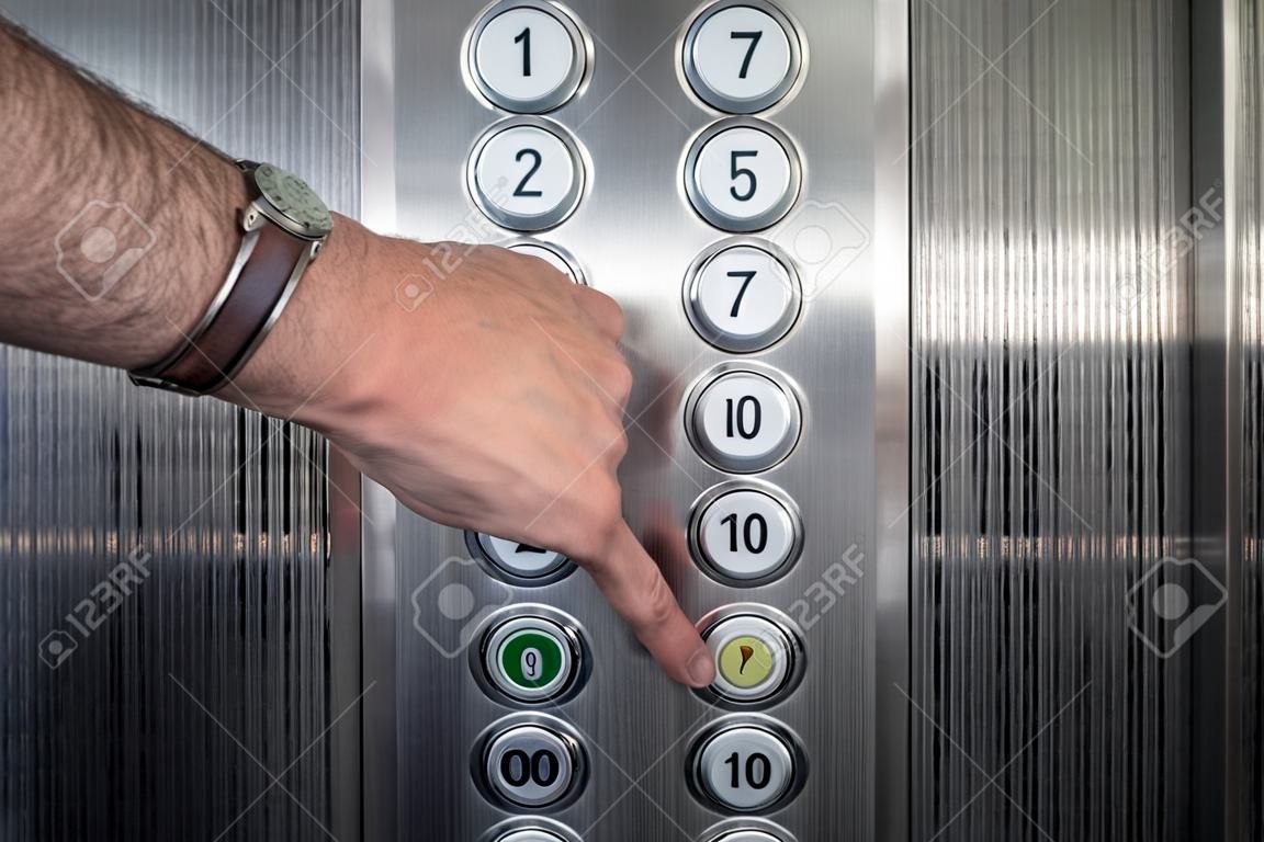 Male forefinger pressing the zero floor button in the elevator. Iron made interior. 
