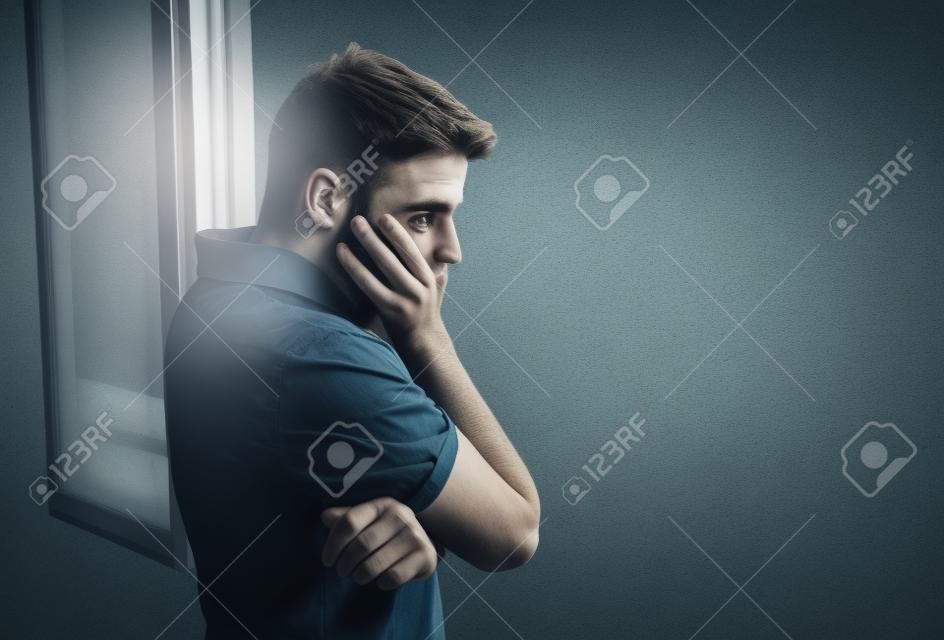 giovane uomo attraente guardando attraverso la finestra con aria preoccupata, depressione depresso sofferenza, riflessivo e solitario in pressione di lavoro o concetto di problemi personali con spazio di copia