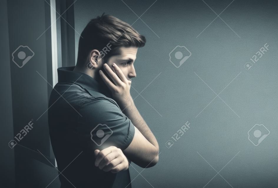 giovane uomo attraente guardando attraverso la finestra con aria preoccupata, depressione depresso sofferenza, riflessivo e solitario in pressione di lavoro o concetto di problemi personali con spazio di copia