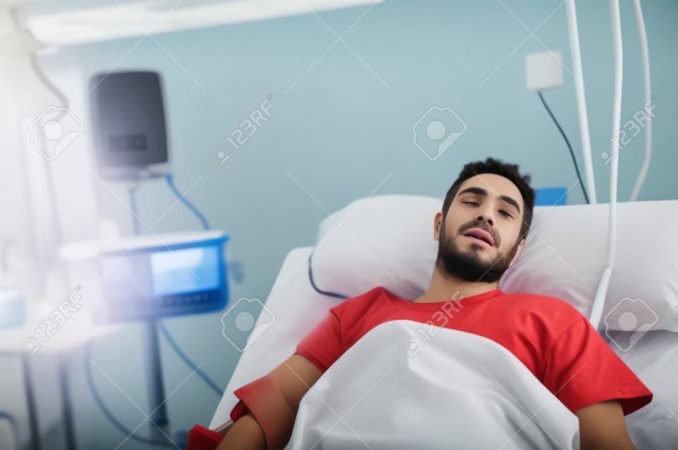 jonge gewonde patiënt man liggend in bed ziekenhuis kamer rust van pijn kijken in slechte gezondheidstoestand na het lijden ongeval in de gezondheidszorg concept