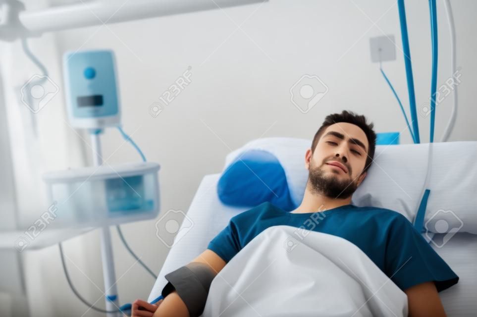 jonge gewonde patiënt man liggend in bed ziekenhuis kamer rust van pijn kijken in slechte gezondheidstoestand na het lijden ongeval in de gezondheidszorg concept