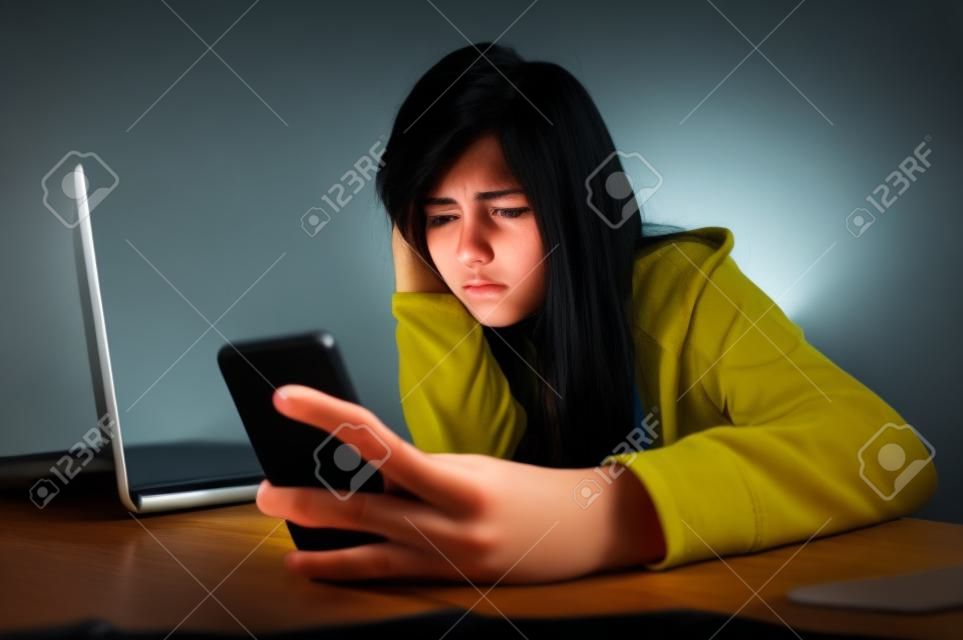 Молодые страшно и беспокоятся подросток девочка с помощью мобильного телефона и ноутбук компьютер в качестве интернет-прошествовал жертвой злоупотреблений и киберзапугивание или киберпреследование концепция стресса в черном фоне