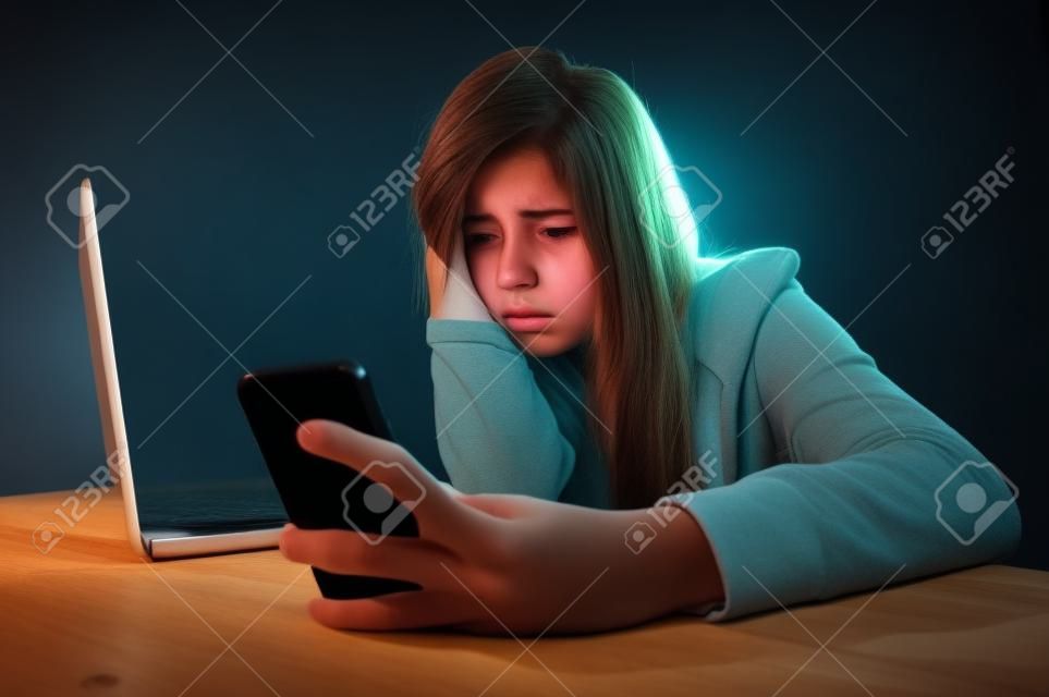 Молодые страшно и беспокоятся подросток девочка с помощью мобильного телефона и ноутбук компьютер в качестве интернет-прошествовал жертвой злоупотреблений и киберзапугивание или киберпреследование концепция стресса в черном фоне