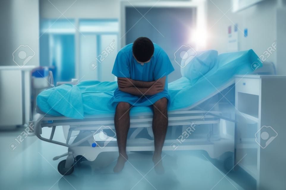 young desperate man sitting at hospital bed alone sad and devastated suffering depression crying at clinic for serious disease diagnose feeling worried and in fear about health
