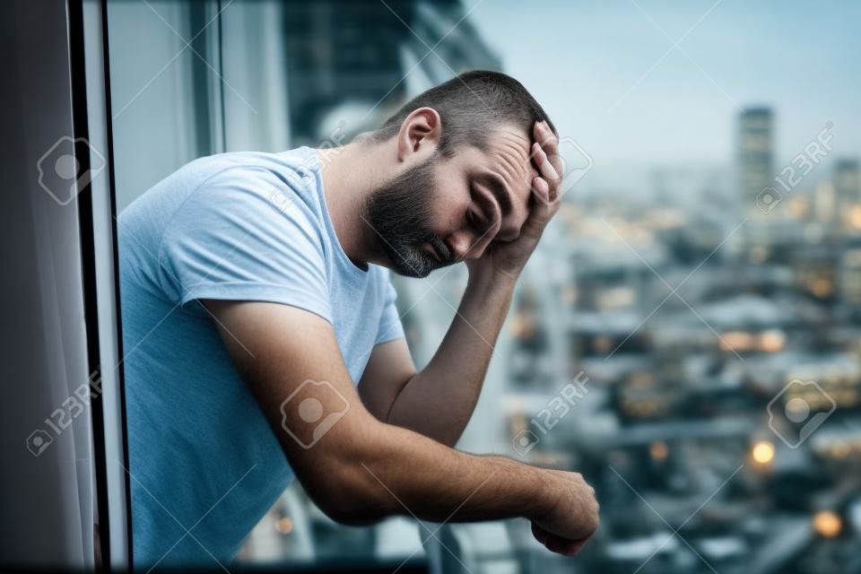 close-up portret van verdrietige en depressieve 40s man kijken door buiten op het thuis balkon eenzaam en attent lijden depressie denken en het gevoel laag in stadsgebouwen stedelijke achtergrond