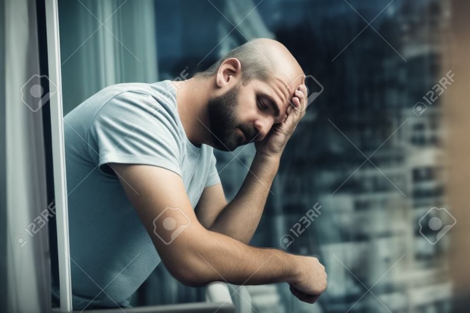 close up retrato de homem triste e deprimido dos anos 40 olhando através do exterior em casa varanda solitário e pensativo sofrendo depressão pensando e sentindo baixo em edifícios da cidade fundo urbano